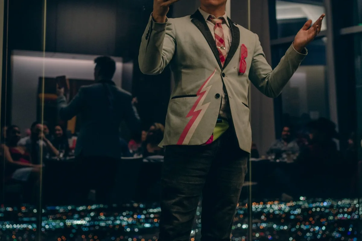 Card trick with a laughing guest, city lights backdrop